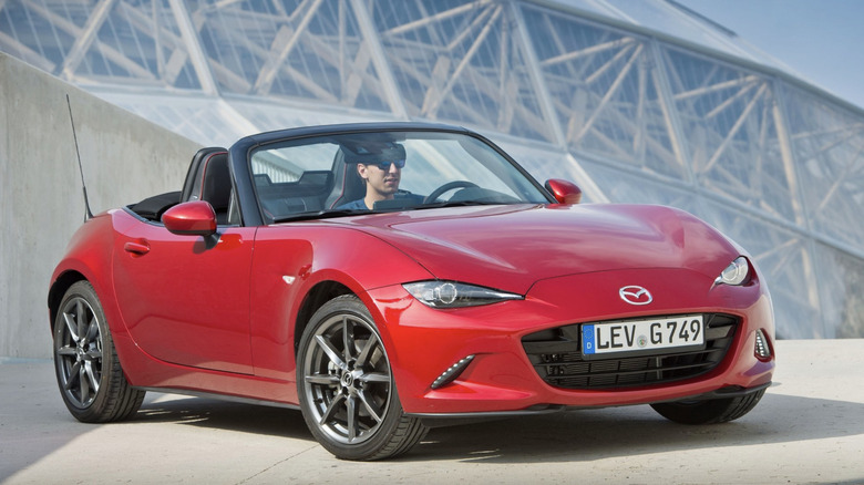 An MX-5 Miata parked on top of a parking garage with an ultra modern building in the background