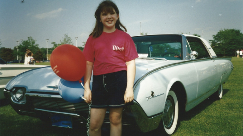 a young girl holding a red ballon in front of a 1961 Ford Thunderbird