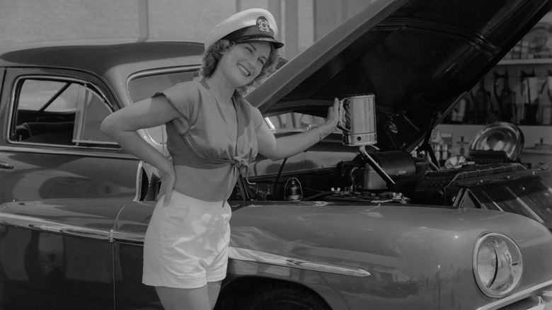 A gal in a captains hat changing oil in her car in the 1950s