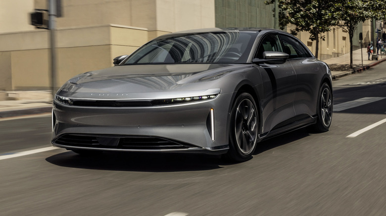 A Lucid Air sedan driving along a city street with trees and buildings behind it