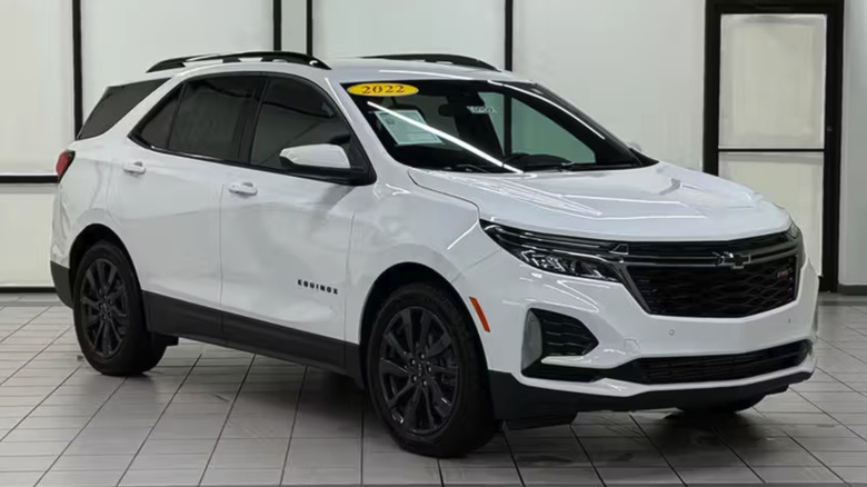 A white Chevrolet Equinox with black wheels on a tile floor and a white wall with metal bars.