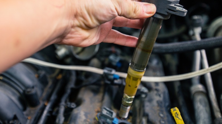 A mechanic holding an ignition coil with a spark plug attached after ejection from the cylinder head.