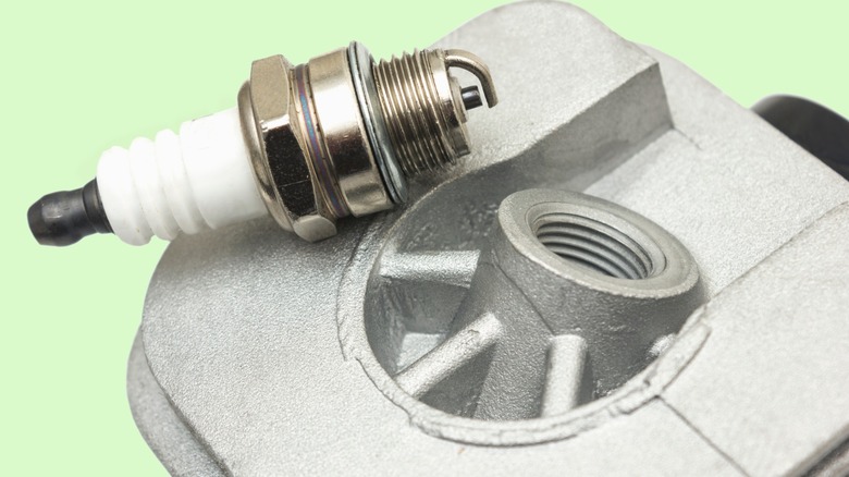 A spark plug placed next to its threaded location on a cylinder head.