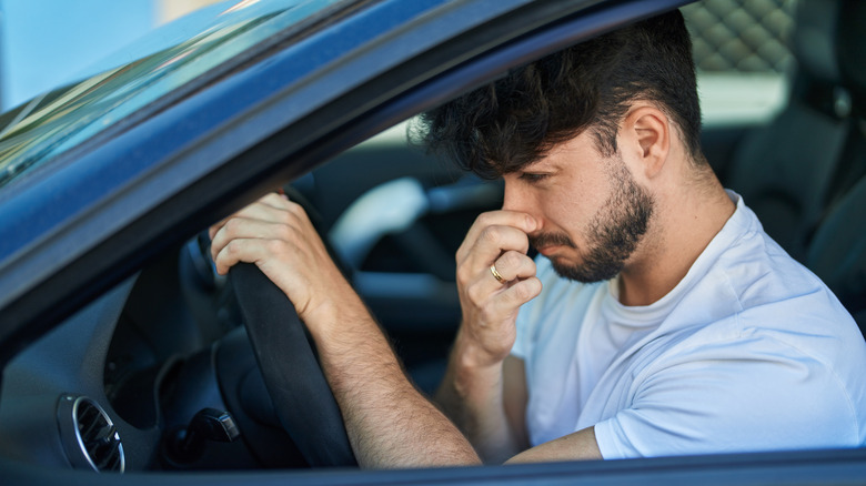A man driving while holding his nose due to an unpleasant smell