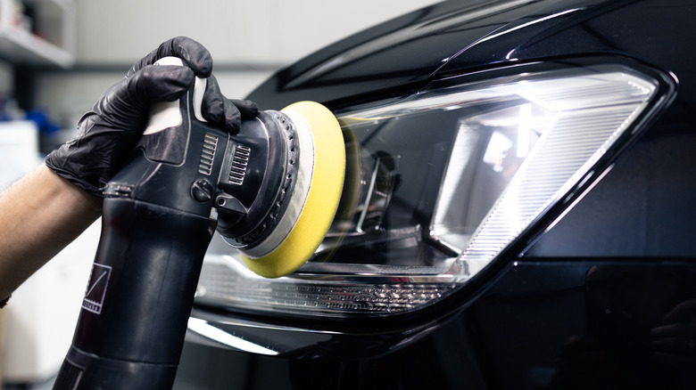 A detailer polishes headlights with an orbital polisher.