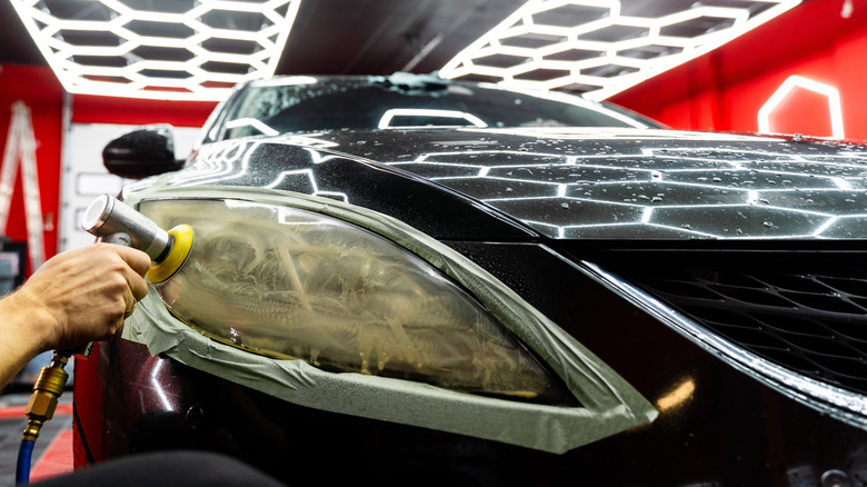 A detailer polishing foggy headlights in a shop.