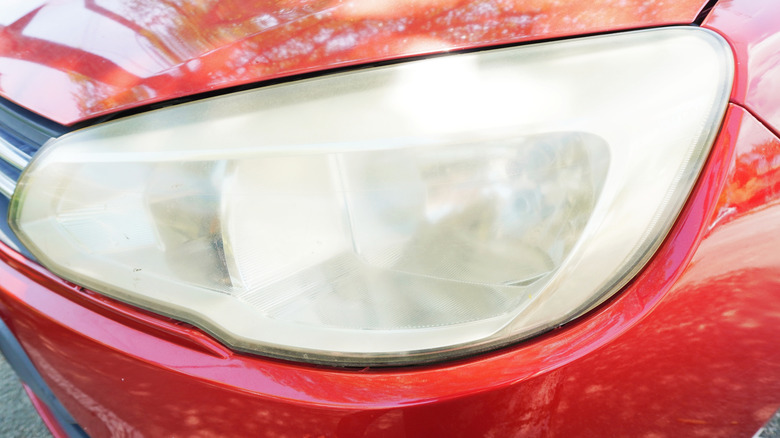 An oxidized headlight on a red car.