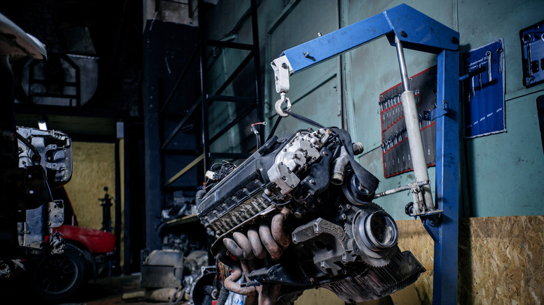 An engine is hoisted up with a blue engine crane inside a workshop.