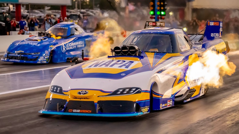 A Funny Car getting off the line with flames coming out, and another car to its left