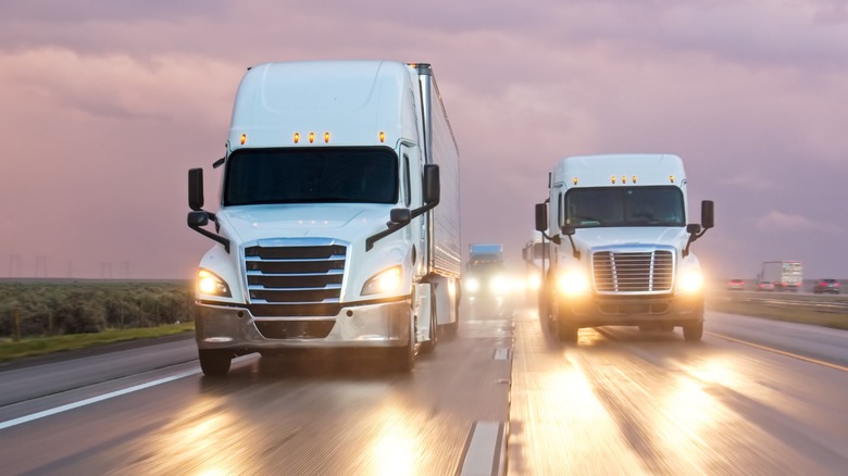 Two white semi-trucks on a highway with lights