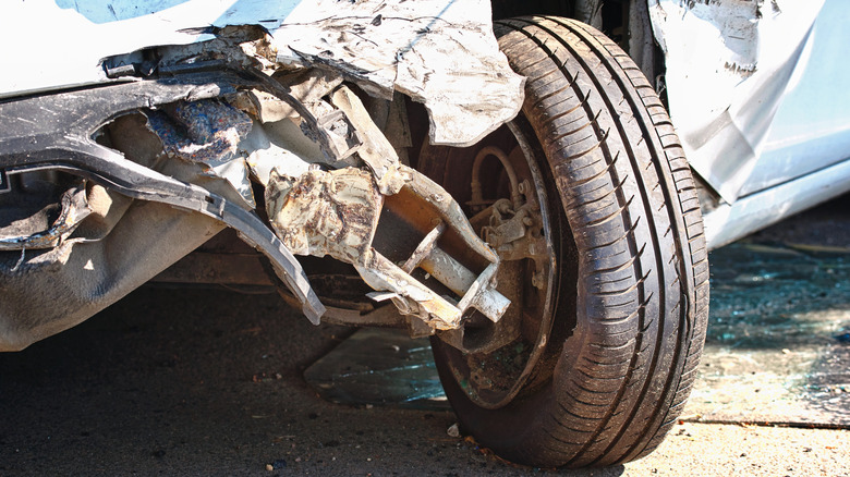 A car with a torn rear wheel and bent axle after a severe road collision.