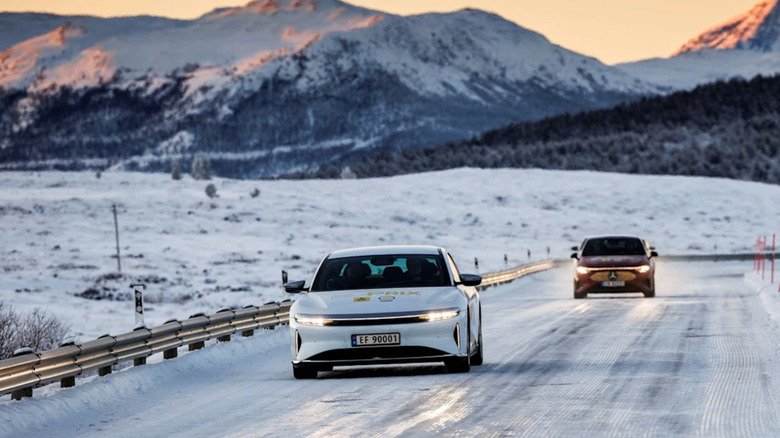 A Lucid Air driving on a snowy roads with a Mercedes-Benz and snowy mountains in the background