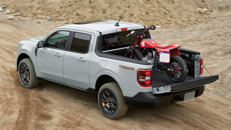 A birds-eye view of a gray Ford Maverick Tremor hauling a dirt bike in its bed while driving.