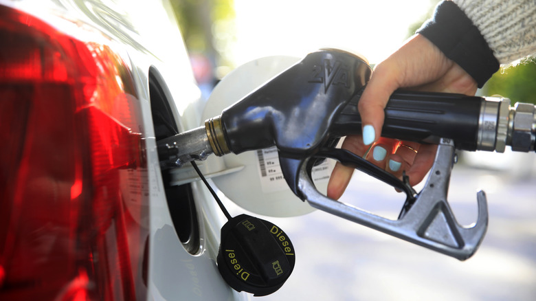 A person filling up a white car with fuel.