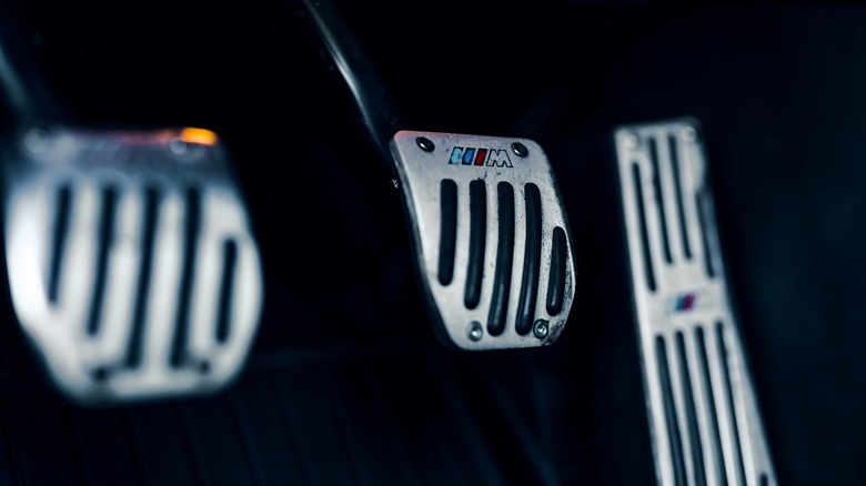 A close-up of a BMW M manual car pedal area showcasing three pedals.