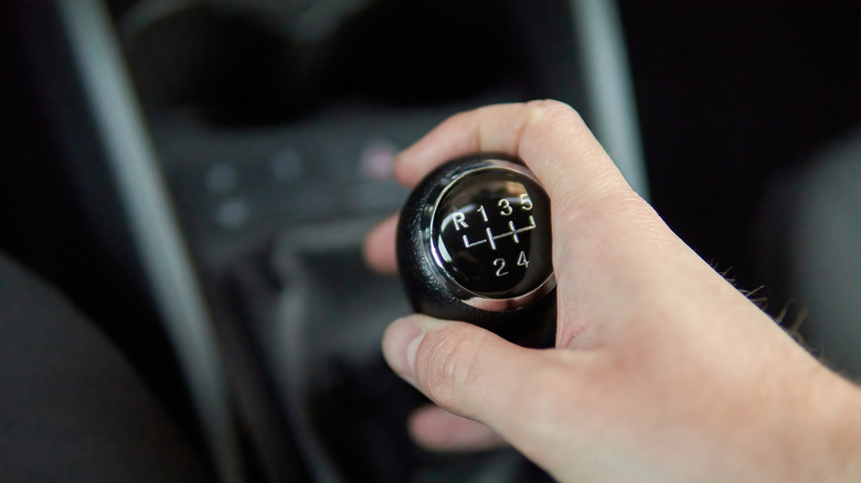 A close-up of a person holding a car manual transmission gear level in its hand.