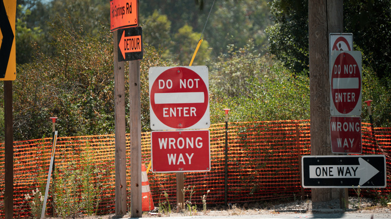 A collection of traffic signs including Do Not Enter, Wrong Way, and Detour are posted near a construction zone with orange safety fencing