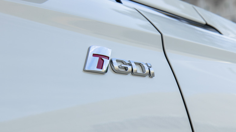 A close-up of a white car's side fender badge saying "TGDi"