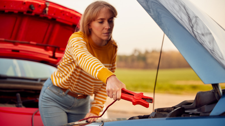 A woman attaching a jumper cable to a car