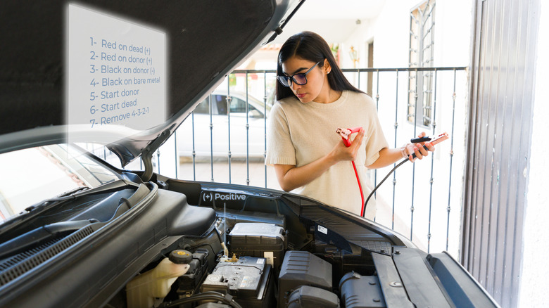 A woman holding jumper cables before jump starting a car