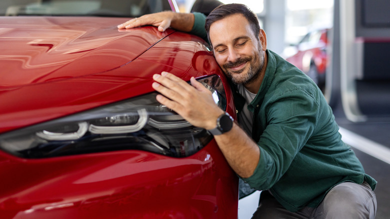 A young man hugging a red Alfa Romeo SUV.