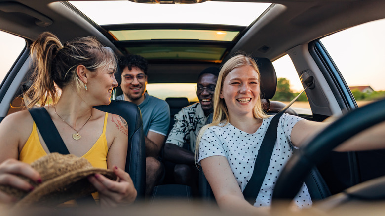 A group of four friends in a small SUV look ready to get on the road for a road trip.