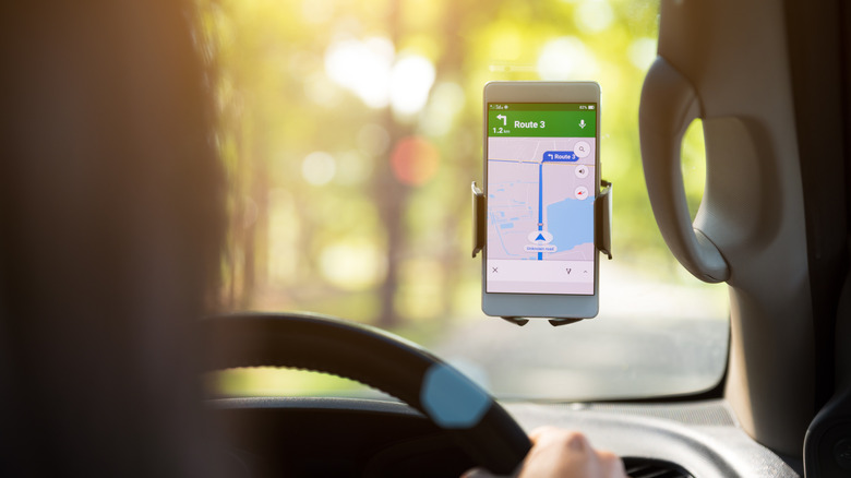 A phone mounted to a windshield shows a route on a map application.