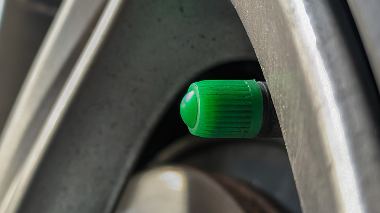 A green valve stem cap on a car's wheel.