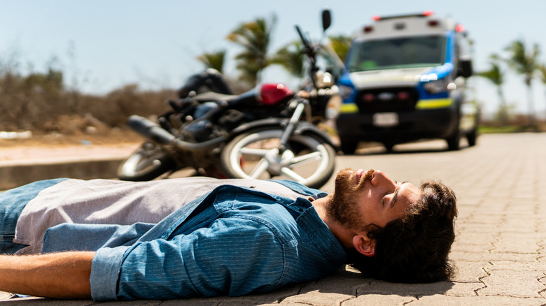 A young man who fainted after a motorcycle accident, with an ambulance arriving in the background