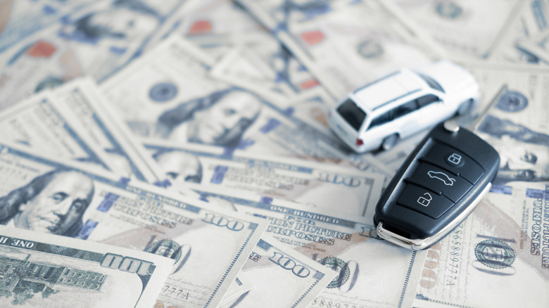 A car key and a scale model of a car placed on a pille of money.