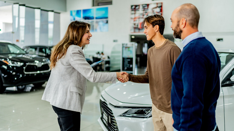 Three people in a car dealership, with two of them shaking hands.