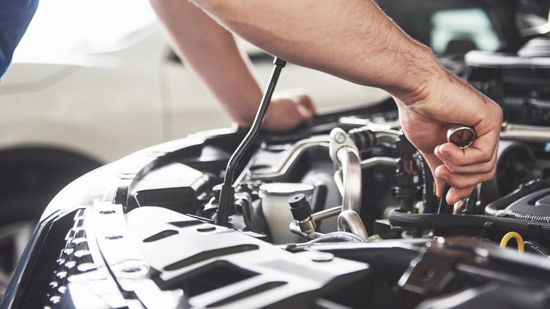 A mechanic's hands holding a wrench while working on a car's engine