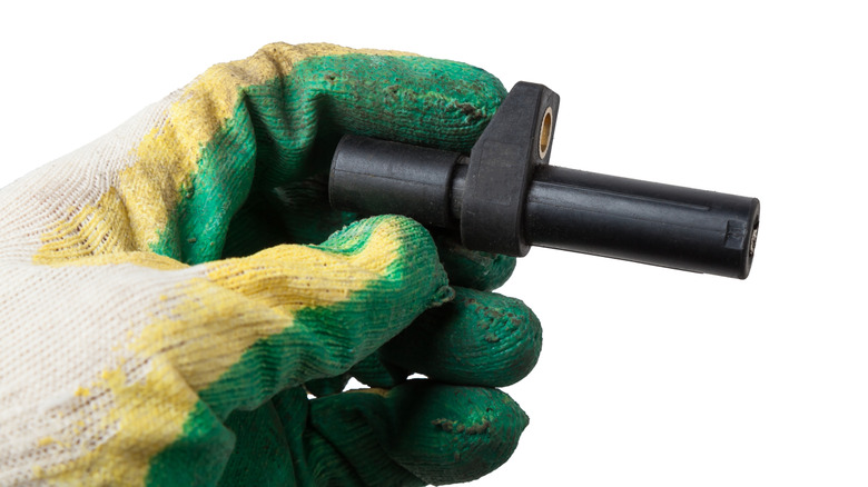 A gloved hand of a mechanic holding a crankshaft position sensor from a car's engine