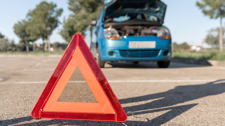 A red warning triangle with a broken car in the background