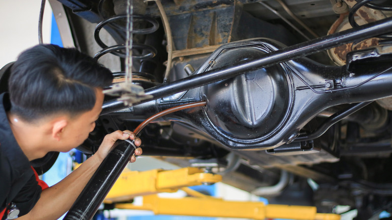 A mechanic adding oil into an off-road car's rear axle differential.