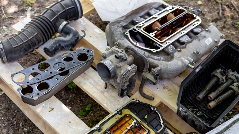 A disassembled internal combustion engine intake and manifold parts laid out on a pallet.