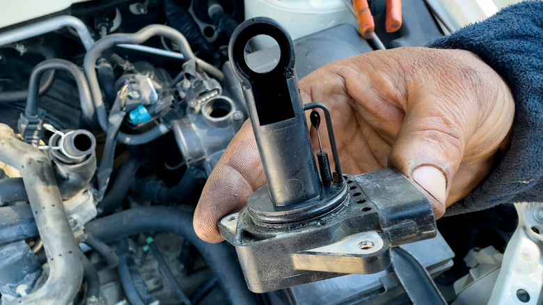 A person holding a manifold absolute pressure sensor above a vehicle's engine bay.