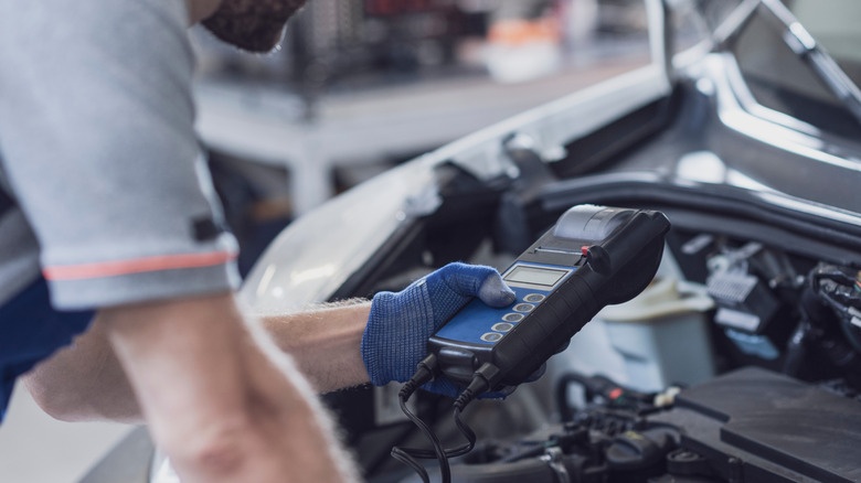 A mechanic holding an OBD-II sensor above a car's engine bay.