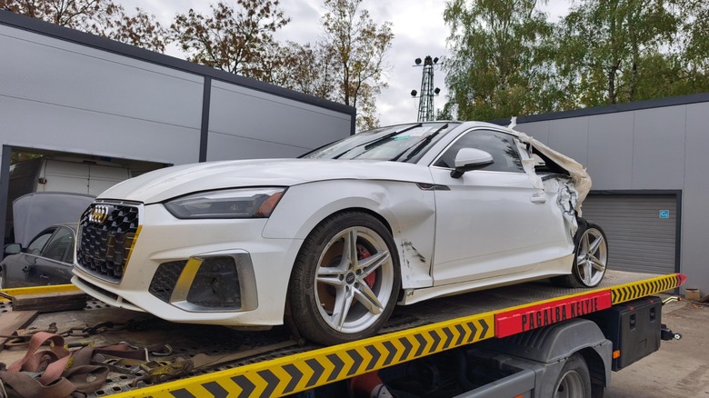 A damaged white Audi on a flatbed truck.