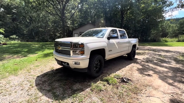a white Chevy Silverado with AFM parked in a patch of dirt in a rural yard