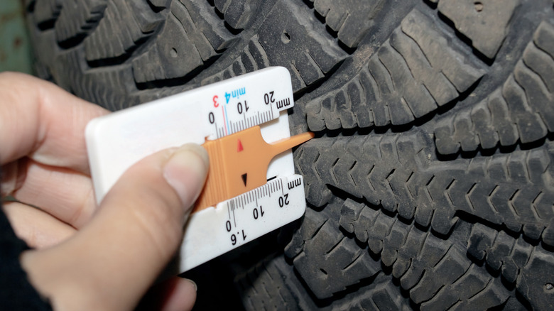 A person is using a ruler to measure the depth of a tire. The tire is likely made of synthetic rubber and designed for road surfaces like asphalt. Keywords Automotive tire, Tread, Finger, Wood, Nail
