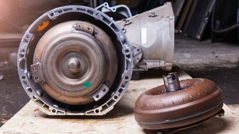 A transmission removed from a car with its torque converter sitting to the side of it.