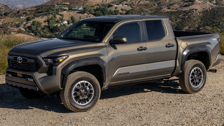 Bronze Oxide Toyota Tacoma TRD Off-Road parked on a gravelly surface with hills and mountains in the background