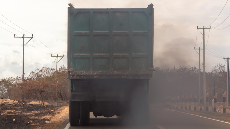 An old diesel truck spewing exhaust smoke as it accelerates on the road