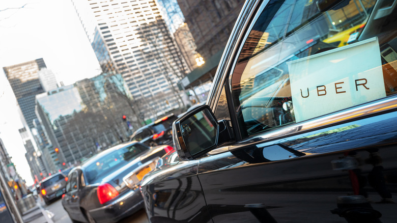 A black car with a white Uber sign in its window sits in New York City traffic.