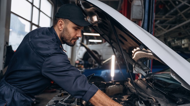 A mechanic working on a car under the hood.