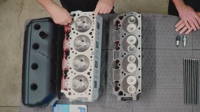 Two sets of hands point out differences in a side-by-side comparison of Hemi and Wedge combustion chambers. Their cylinder heads rest on a workbench