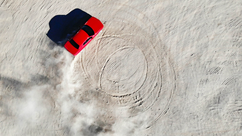 A modern red Dodge Challenger spins donuts in the sand