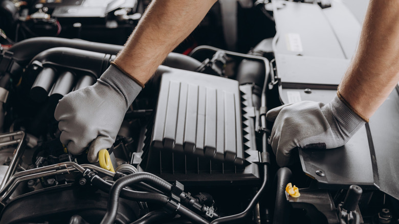 The gloved hands of a mechanic servicing a car engine