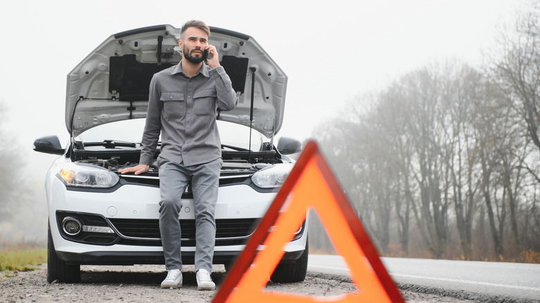 A man calling for recovery in front of a broken Renault Megane